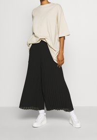 Beige oversized T-shirt met korte mouwen, gecombineerd met zwarte plooienwijdte broek en witte sneakers, met een textuurrijke, zachte stof.