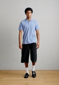 Ανοιχτό γαλάζιο πόλο με κοντά μανίκια, μαύρες σορτς σε άνετη γραμμή, άσπρες κάλτσες και μαύρα μοκασίνια. Αποπνέει ένα casual, μονοχρωματικό στυλ.