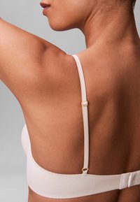 Lichtroze bh van gladde stof, met dunne bandjes en een subtiel gouden gespje aan de achterkant.