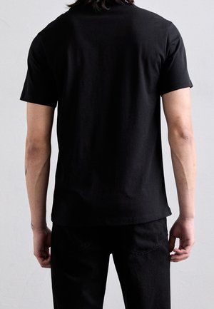 Czarna koszulka z krótkim rękawem wykonana z bawełny, z prostym wzorem i prostym dołem, noszona z ciemnymi dżinsami, widok od tyłu.