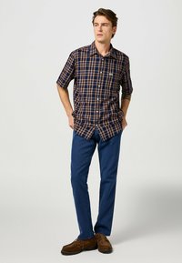 Korte mouwen geruite overhemd in marineblauwe en bruine tinten, knopenlijst aan de voorkant, klassieke kraag, gecombineerd met een blauwe broek en bruine schoenen.