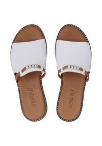 White slide sandals with a brown base, featuring crystal accents and a textured strap. Brown sole with decorative studs along the edge.