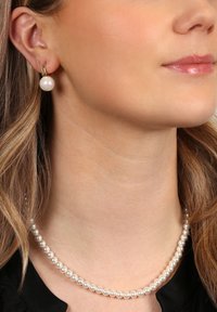 Pärlhalsband och en enkel pärlörhänge, båda med en blank yta. Halsbandet har jämnstora pärlor, och örhänget har guldförstärkningar.