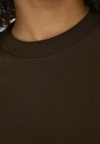 Maglione a girocollo in cotone marrone con texture liscia e scollatura a costine, mostrato da vicino per evidenziare i dettagli del tessuto.