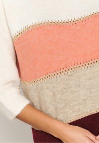 Neulepusero, jossa on värilohkodesign kermaan, koralliin, beigeen ja viininpunaiseen, koristeellisella pitsireunuksella saumoissa.