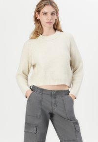 Maglione corto a coste color crema con maniche lunghe, abbinato a pantaloni cargo grigi con multiple tasche e chiusura a bottone.