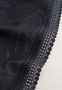 Gros plan sur un tissu noir avec des motifs texturés subtils et une bordure en dentelle décorative le long du bord sur un fond clair.