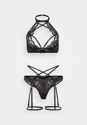 Set di lingerie in pizzo nero con bralette a incrocio sulla schiena e perizoma abbinato con reggicalze e dettagli in metallo color oro.