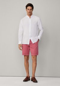 Witte linnen overhemd met een mandarin-kraag, gecombineerd met roze shorts. Bruine leren instappers maken de look compleet.
