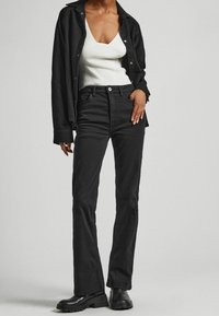 Jeans a zampa neri in denim con vita alta, abbinati a una canotta bianca a coste e a un giubbotto oversize nero, con stivaletti chunky neri.