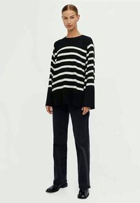 Maglione a righe bianche e nere con un fit rilassato, maniche lunghe e collo a giro, abbinato a pantaloni scuri e scarpe lucide.
