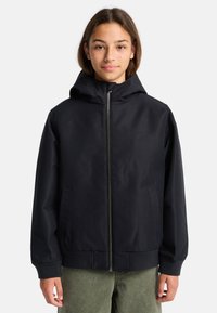 Giacca nera con cappuccio, zip frontale, tasche laterali e polsini a coste. Presenta un logo discreto sul petto e una texture liscia.