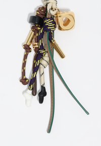 Llavero con varios cordones texturizados en marrón, verde, negro y púrpura, con un charm cuadrado dorado y nudos de varios colores.