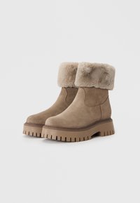 Bottines en daim marron avec un revers en fausse fourrure, semelle en caoutchouc épaisse, détails texturés et un design à bout rond.