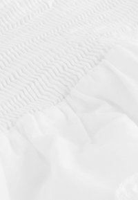 Hvid tekstil med indviklede smock-detaljer på én sektion og blød samlet stof på en anden, begge med en glat tekstur.