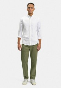 Vit långärmad skjorta med knappar, gröna byxor och krämfärgade sneakers. Kragsdesign med knäppning och uppvikta ärmar.