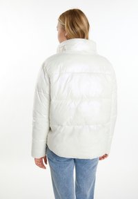Hvid polstret jakke med glat finish, høj krave og sydde paneler. Båret med lyseblå denim, som viser et cozy men struktureret design.