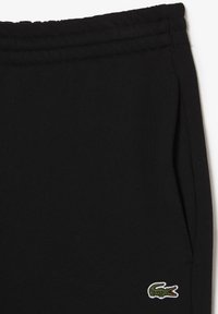 Svarta sweatpants i mjuk bomull med elastisk midja, med en liten grön och vit broderad krokodil-logotyp på sidan.