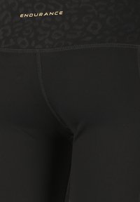 Svarta träningsleggings med en slät yta, midjeband med leopardmönster och en guld "ENDURANCE"-logotyp på framsidan.