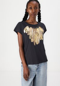 Black short-sleeve t-shirt in cotton with a glossy gold feather design across the chest. Soft texture, relaxed fit, and rounded neckline.