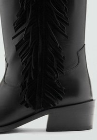 Gheată de gleznă din piele neagră, cu detaliu proeminent cu franjuri negri pe lateral, toc suprapus și textură netedă.