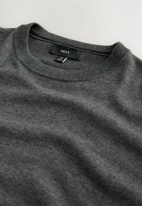 Sudadera gris con escote redondo, cuello de canalé y etiqueta que muestra "NEXT" y talla "M". Textura suave, diseño de punto liso.