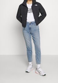 Black puffer jacket with a zip closure and high collar, worn over a white t-shirt, paired with light blue jeans and mixed-color sneakers.