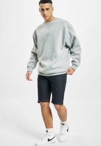 Harmaa fleece-sweatshirt, jossa on pyöreä kaula-aukko, yhdistetty tummiin farkkushortseihin. Valkoiset high-top lenkkarit. Rentoa tyyliä ja mukava design.