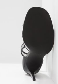 Svart högklackad sandal med tunna remmar, spetsig tå och en smal stilettklack. Slät läderöverdel med en texturerad sula.