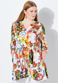 Tunika a V con maniche 3/4, caratterizzata da una vivace stampa di frutta e fiori su sfondo bianco, con tasche laterali.