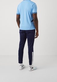 Vaaleansininen urheilupaita tummansinisin yksityiskohdin, yhdistetty tummansinisiin juoksuhousuihin, joissa valkoiset raidat sivuilla, nähtynä takaa.