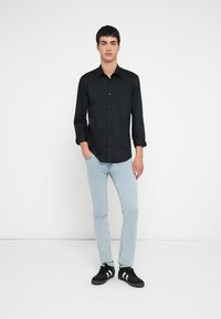 Schwarzes Button-up-Hemd mit langen Ärmeln, hellblaue Jeans und schwarze Sneakers mit weißen Streifen. Einfaches Design, glatte Stofftextur.