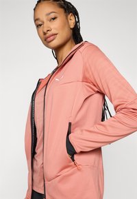 Heled roosa tõmblukuga jakk tekstuuriga disainiga, mustade detailidega, küljetaskudega, sobiva siluetiga ja väike logo rinnal.