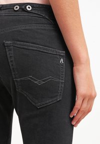 Svart jeans med hög midja och två metallknappar. Bakfickan har ett distinkt broderat zigzag-mönster.