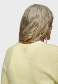 Maglione giallo lavorato a maglia con una morbida texture pelosa; presenta un piccolo numero ricamato "10" sulla parte posteriore.