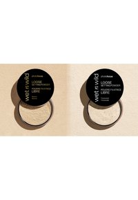 Losse fixeerpoeder in twee containers. Elk heeft een ronde zwarte dop met gouden tekst. Eén variant is gelabeld als "Banaan", de andere als "Transparant".