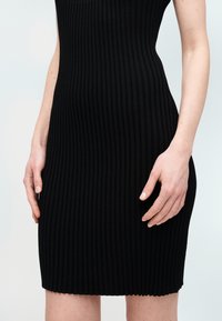 Μαύρο εφαρμοστό φόρεμα με ριγέ υφή, μήκους μέχρι το γόνατο. Υλικό με κάθετες ρίγες. Αμάνικο σχέδιο. Χέρια τοποθετημένα κοντά στην περιοχή της μέσης.