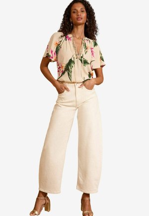 Blusa floreale a maniche corte con scollo a V e dettagli con lacci, abbinata a pantaloni a vita alta larghi color crema e sandali con tacco dorati.