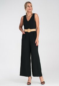 Czarny bezrękawnik z dekoltem w kształcie litery V, z wyszczuploną talią i beżowym plecionym paskiem. Luźne szerokie nogawki i fakturowany materiał.