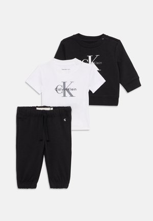 Due pantaloni neri con polsini elasticizzati e coulisse, maglietta bianca a maniche corte con logo Calvin Klein e maglietta nera a maniche lunghe con logo.