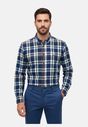 Camisa de hombre de botones en patrón a cuadros en tonos azul marino, verde y blanco, con cuello y mangas largas, combinada con pantalones azules.