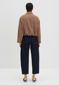 Bruine cropped jas met een relaxed fit en een kraag, gecombineerd met donkerblauwe wijde jeans, van achteren weergegeven. Eenvoudig ontwerp, minimale details.