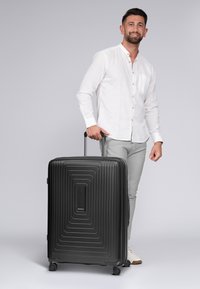 Maleta rígida negra con un diseño acanalado, mango extensible y cuatro ruedas giratorias. Tamaño compacto con forma rectangular.