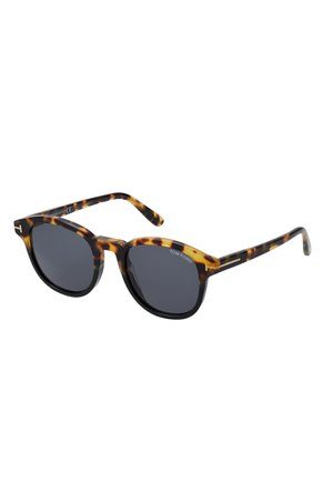 Occhiali da sole tartarugati con lenti scure e montatura arrotondata, caratterizzati da un accento a doppia barra e dal logo "TOM FORD" sulle tempie.