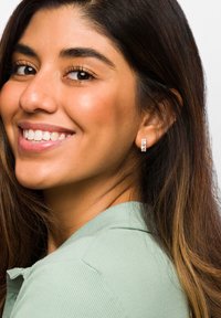 Runda silverörhängen med en klar stendetalj, bärs av en person med långt, mörkt hår, klädd i en ljusgrön skjorta.