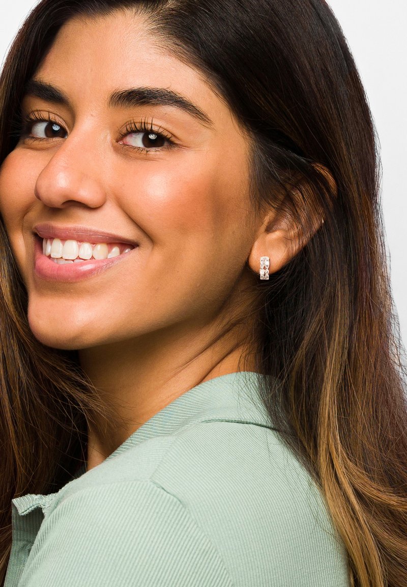 Runda silverörhängen med en klar stendetalj, bärs av en person med långt, mörkt hår, klädd i en ljusgrön skjorta.