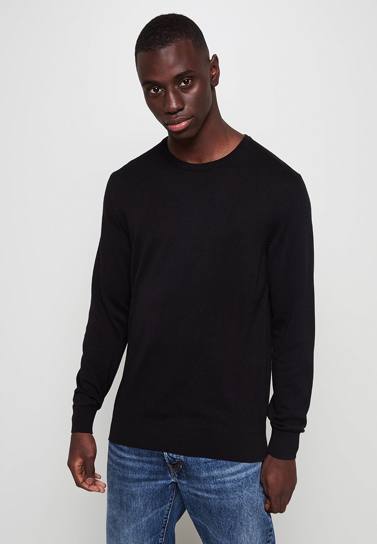 Schwarzer Strickpullover mit rundem Ausschnitt, langen Ärmeln und gerippten Bündchen. Kombiniert mit blauen Jeans, verfügt über einen strukturierten Stoff.