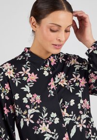 Camisa negra de botones con un patrón floral en rosa, blanco y verde. Tela suave con un cuello clásico y puños abotonados.