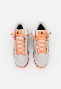 Zapatillas deportivas gris con cordones y acentos naranjas. Tejido texturizado y suela de goma. Logo notable en la lengua.