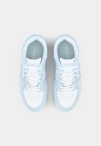 Baskets blanches et bleu clair avec embout perforé, fermeture à lacets, semelle épaisse et logo "Lacoste" sur le côté. Texture en cuir lisse.